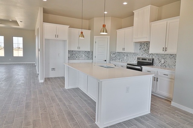 kitchen with wood finish floors, white cabinets, stainless steel electric range, tasteful backsplash, and an island with sink