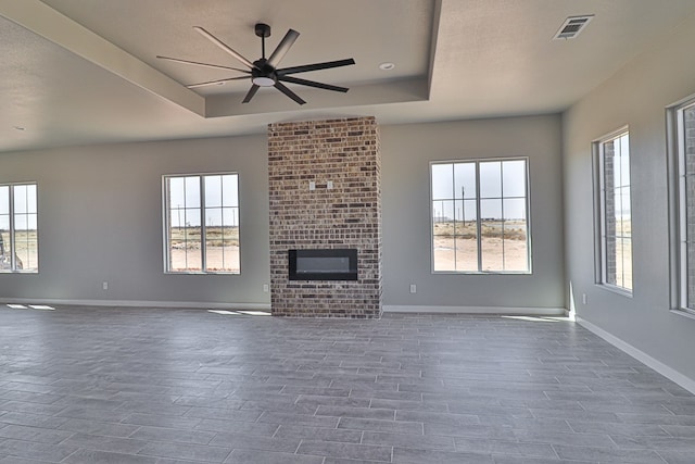 unfurnished living room featuring visible vents, a healthy amount of sunlight, baseboards, a brick fireplace, and a tray ceiling