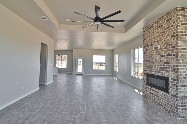 unfurnished living room featuring a brick fireplace, baseboards, visible vents, and wood finished floors