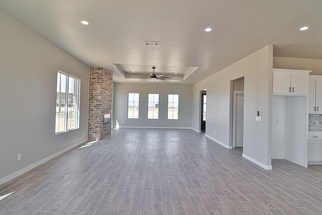 unfurnished living room featuring plenty of natural light, light wood-type flooring, and a raised ceiling