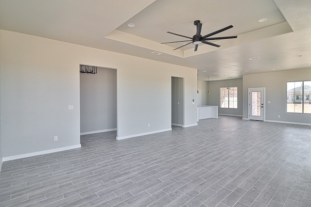 unfurnished living room featuring a ceiling fan, a tray ceiling, baseboards, and wood finished floors