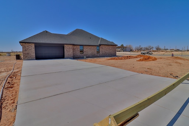 view of front facade featuring a shingled roof, concrete driveway, brick siding, and an attached garage