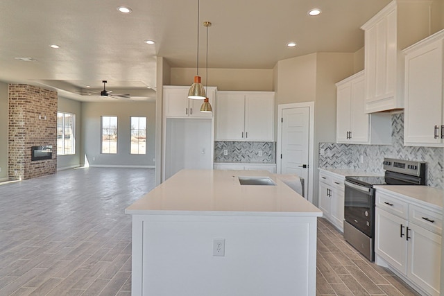 kitchen with electric range, wood finish floors, a fireplace, and a kitchen island with sink