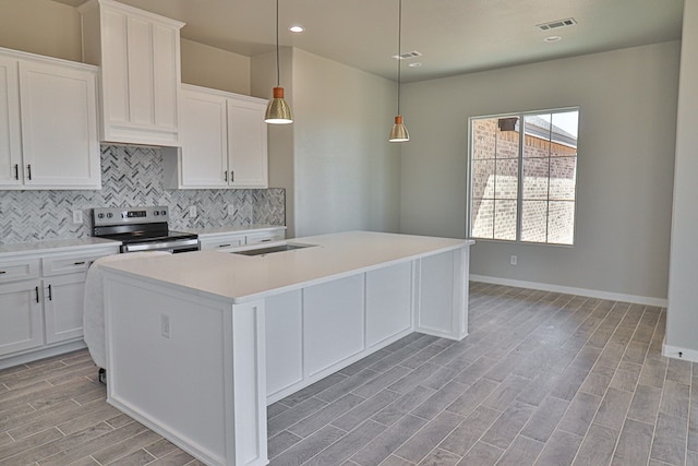 kitchen featuring tasteful backsplash, light countertops, electric range, wood tiled floor, and a kitchen island with sink