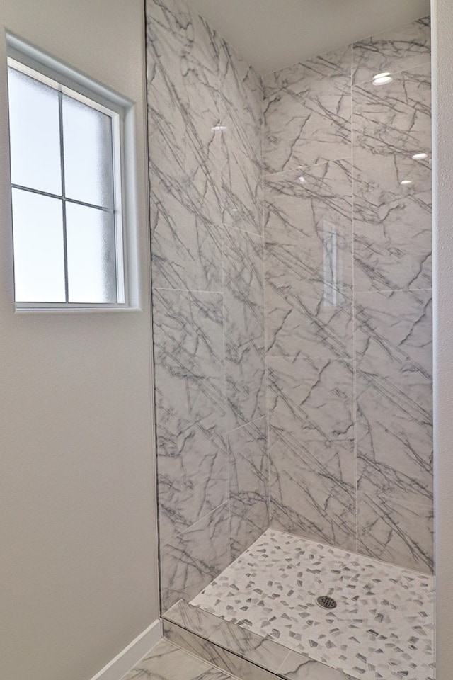 bathroom with marble finish floor, a tile shower, and baseboards