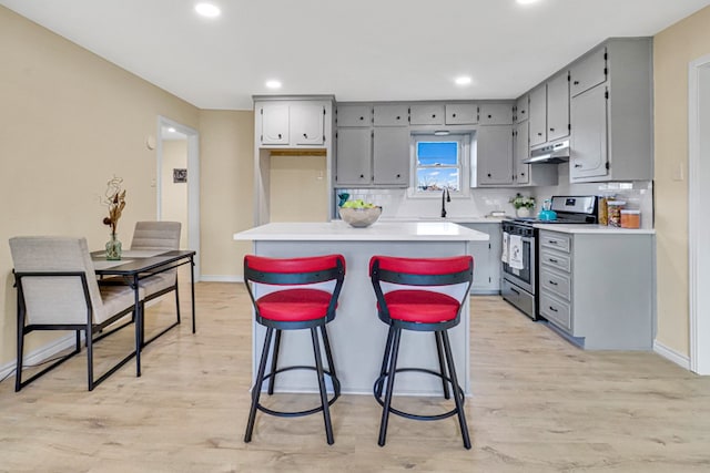 kitchen with stainless steel range with gas cooktop, backsplash, under cabinet range hood, and gray cabinetry