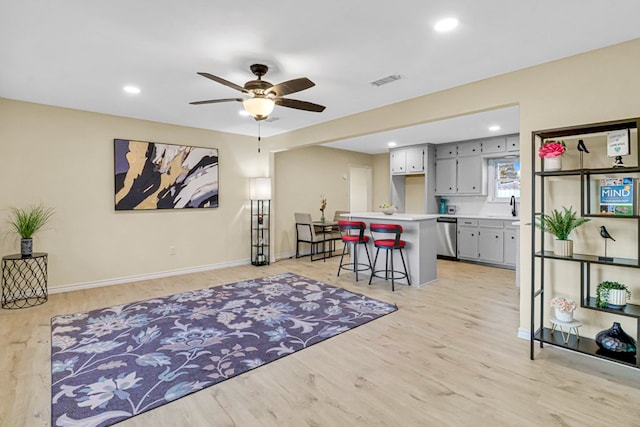 kitchen featuring light countertops, light wood-style flooring, gray cabinetry, stainless steel dishwasher, and a kitchen bar