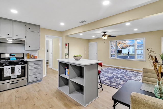 kitchen with light wood finished floors, visible vents, open floor plan, stainless steel range with gas stovetop, and under cabinet range hood