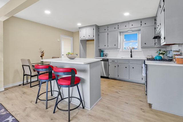 kitchen featuring light wood-style flooring, under cabinet range hood, a sink, appliances with stainless steel finishes, and gray cabinets