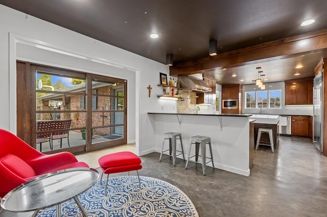 interior space with a breakfast bar area, appliances with stainless steel finishes, kitchen peninsula, pendant lighting, and wall chimney range hood