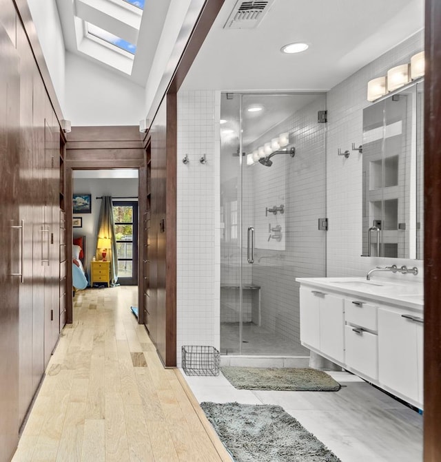 bathroom featuring an enclosed shower, vanity, lofted ceiling with skylight, and hardwood / wood-style floors