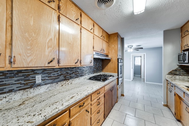 kitchen featuring a textured ceiling, appliances with stainless steel finishes, ceiling fan, backsplash, and light stone counters