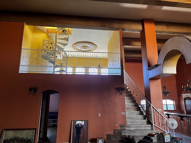 staircase featuring beamed ceiling and a high ceiling