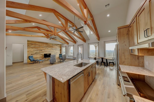 kitchen with light stone countertops, appliances with stainless steel finishes, light wood-type flooring, sink, and an island with sink