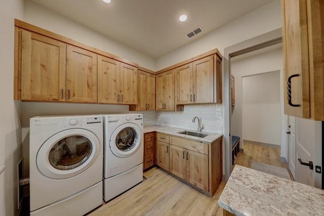 clothes washing area featuring cabinets, washing machine and dryer, light hardwood / wood-style flooring, and sink