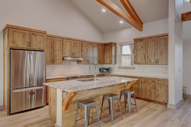 kitchen with sink, stainless steel appliances, light stone counters, light hardwood / wood-style flooring, and a kitchen island with sink