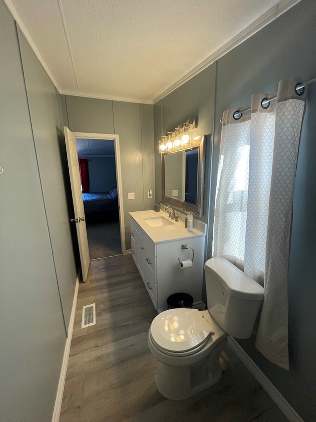 bathroom featuring vanity, toilet, ornamental molding, a textured ceiling, and wood-type flooring