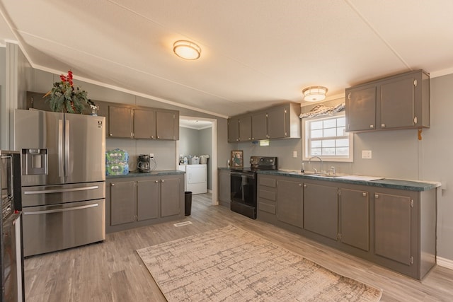 kitchen featuring stainless steel fridge, washer and clothes dryer, sink, light hardwood / wood-style floors, and black / electric stove