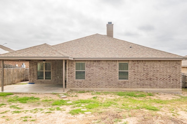 rear view of house with a shingled roof, a patio area, brick siding, and a fenced backyard