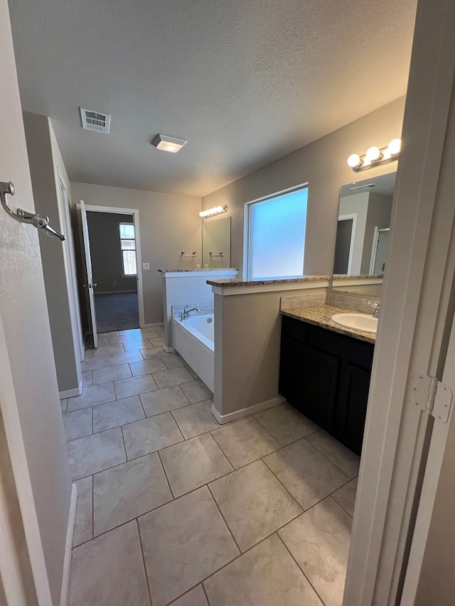 bathroom with tile patterned floors, a bathing tub, vanity, and a textured ceiling