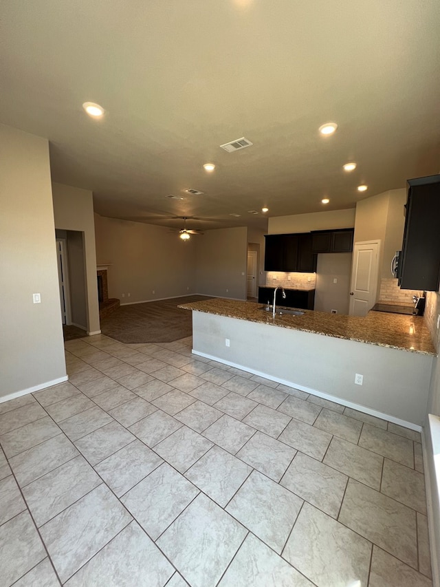 kitchen featuring kitchen peninsula, decorative backsplash, light stone counters, ceiling fan, and sink