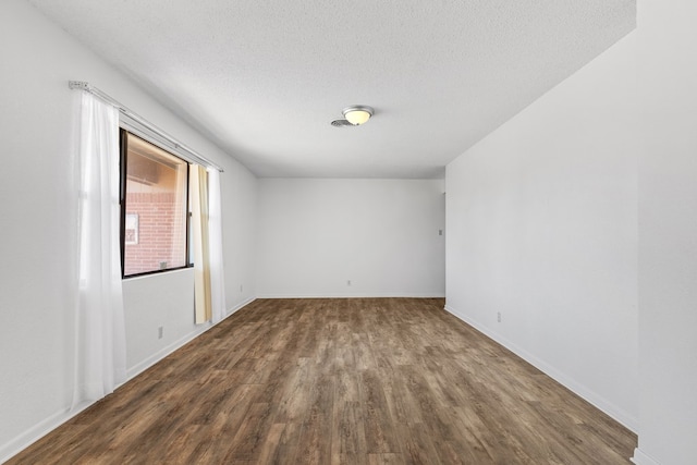 empty room with a textured ceiling and dark hardwood / wood-style floors