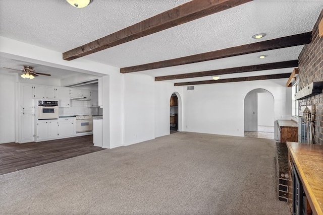 unfurnished living room featuring ceiling fan, a fireplace, a textured ceiling, and dark colored carpet