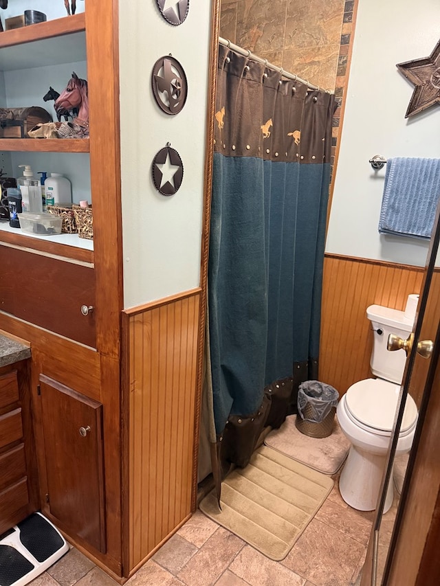 bathroom with wooden walls, toilet, vanity, and a shower with shower curtain