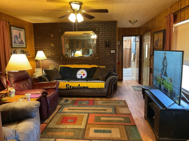 living room featuring wooden walls, dark hardwood / wood-style flooring, ceiling fan, and brick wall