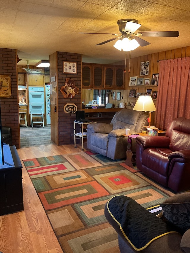 living room featuring ceiling fan, wooden walls, hardwood / wood-style floors, and brick wall