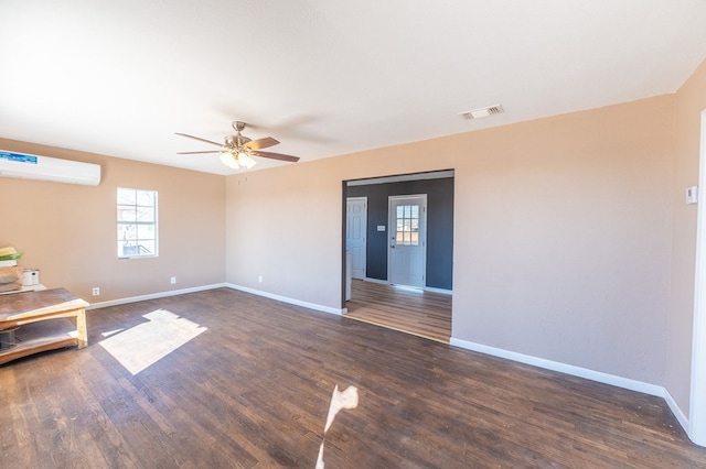 empty room with dark hardwood / wood-style flooring, a wall unit AC, and ceiling fan