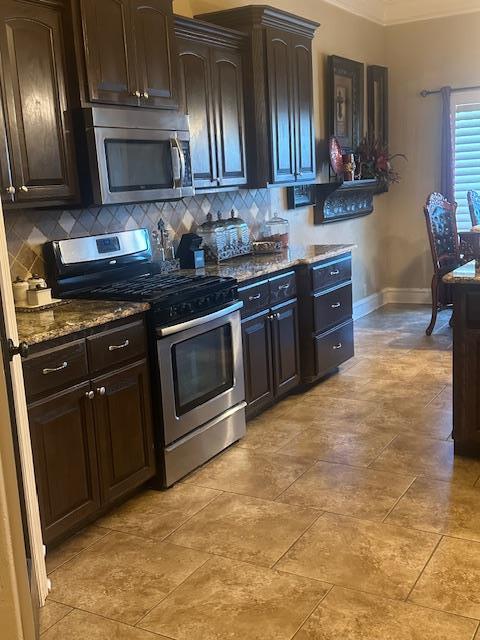 kitchen with dark stone countertops, tasteful backsplash, dark brown cabinetry, and stainless steel appliances