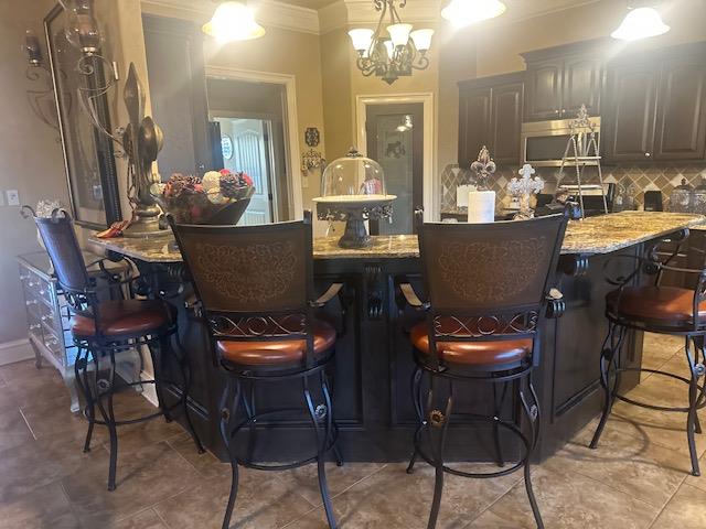 bar featuring decorative backsplash, stainless steel microwave, ornamental molding, and a chandelier