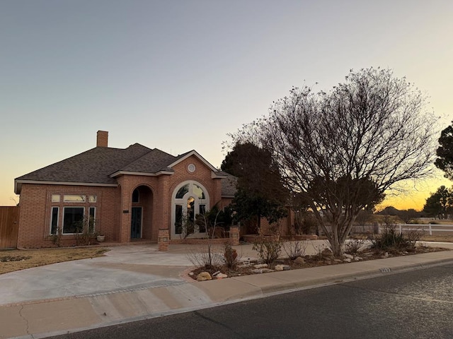 view of front of home with brick siding, fence, driveway, roof with shingles, and a chimney