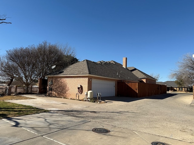 view of side of home featuring brick siding, fence, driveway, and an attached garage