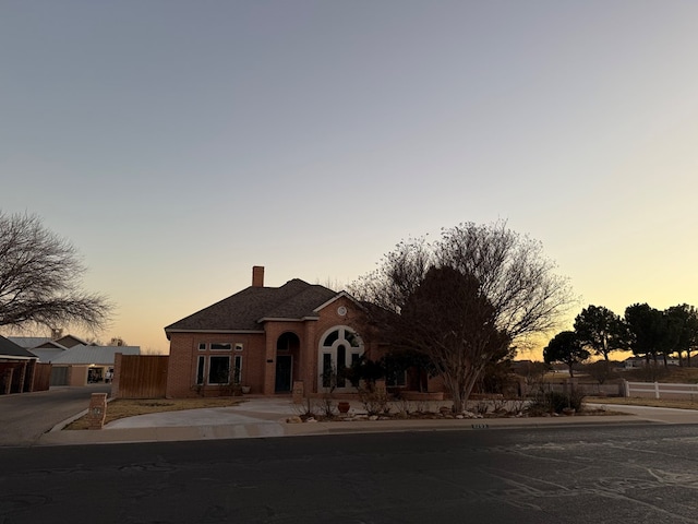 view of front of house with brick siding, fence, and a chimney