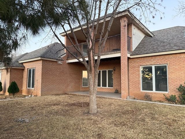 rear view of house featuring a balcony, brick siding, a shingled roof, and a patio