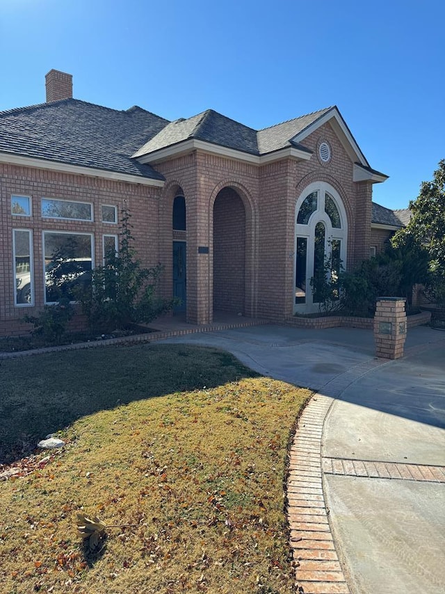 view of front of property featuring brick siding, a chimney, a shingled roof, and a front lawn