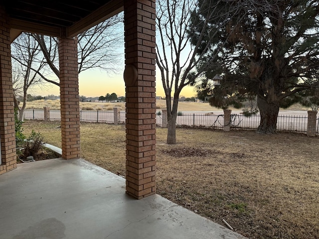 patio terrace at dusk featuring a fenced backyard and a yard