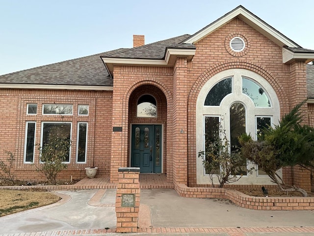 doorway to property featuring french doors, brick siding, a chimney, and roof with shingles