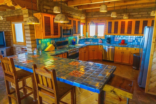 kitchen with appliances with stainless steel finishes, tile countertops, hanging light fixtures, and sink