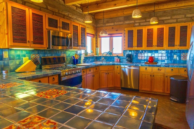 kitchen featuring appliances with stainless steel finishes, sink, pendant lighting, beam ceiling, and tile counters