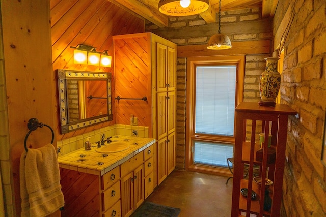 bathroom with concrete flooring, beam ceiling, wood walls, and sink