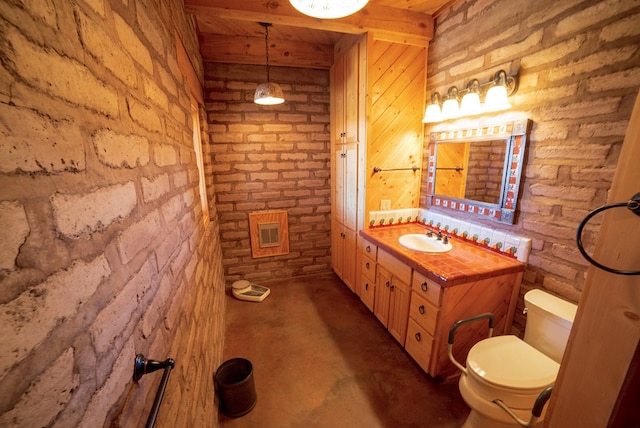 bathroom featuring concrete flooring, vanity, brick wall, and toilet