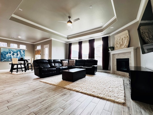 living room with ornamental molding, wood finished floors, a raised ceiling, a brick fireplace, and ceiling fan