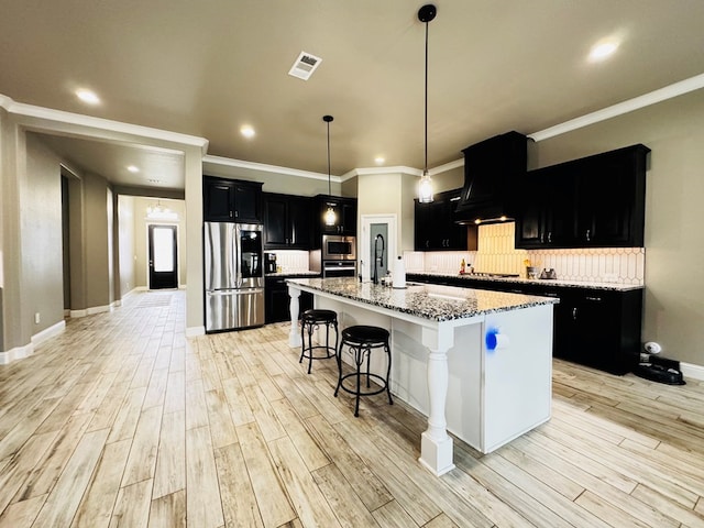 kitchen with premium range hood, visible vents, stainless steel appliances, decorative backsplash, and dark cabinets