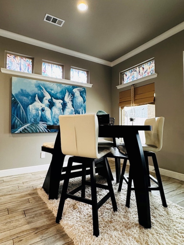 dining room featuring baseboards, wood finished floors, visible vents, and ornamental molding