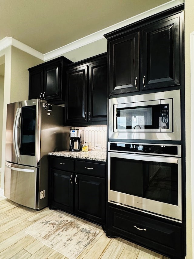 kitchen featuring light wood-style flooring, backsplash, dark cabinetry, appliances with stainless steel finishes, and crown molding