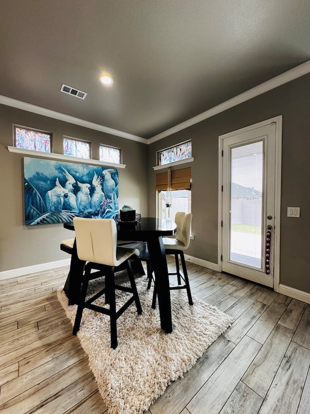 dining space featuring crown molding, baseboards, visible vents, and light wood finished floors