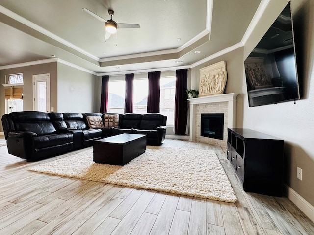 living room with baseboards, wood finished floors, a glass covered fireplace, a raised ceiling, and a ceiling fan